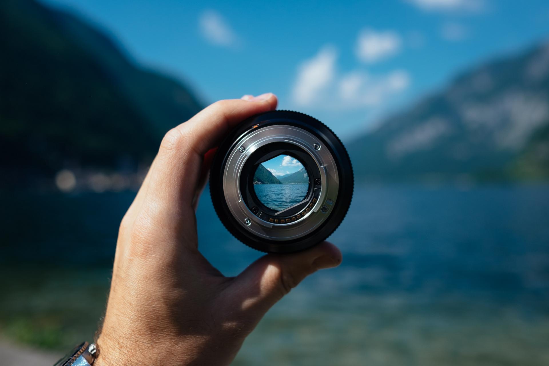 Hand holding lens on the backdrop of a lake - everything is blurred except what is focused by the lens, which is clear